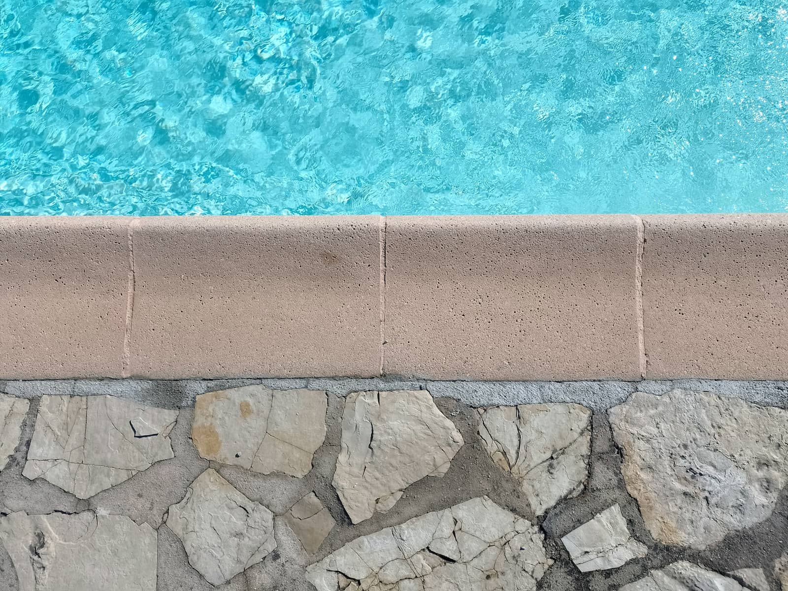 Turquoise pool water meeting new bullnose coping and irregular flagstone decking, seen from above.